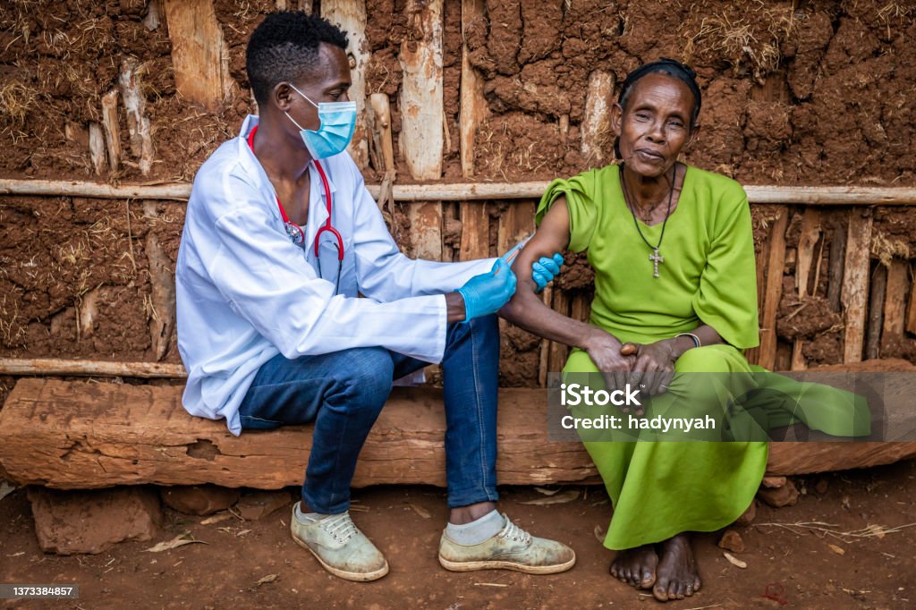 Doctor is doing an injection to senior African woman in small village, East Africa Male doctor vaccinating senior African woman in small village, East Africa. Africa Stock Photo