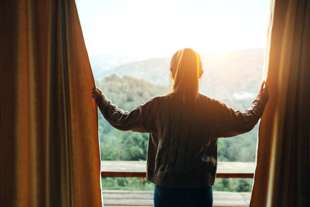 le tende di apertura della donna godono della vista sulle montagne al mattino, il viaggiatore felice soggiorno in hotel. - waking up window women morning foto e immagini stock