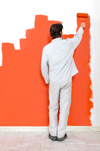 Man, painting a wall with orange paint and a paint roller