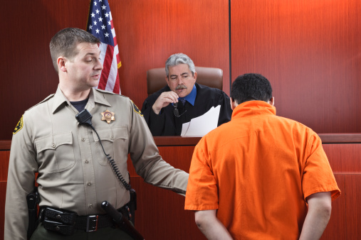 Male judge speaking to a prisoner in the courtroom.