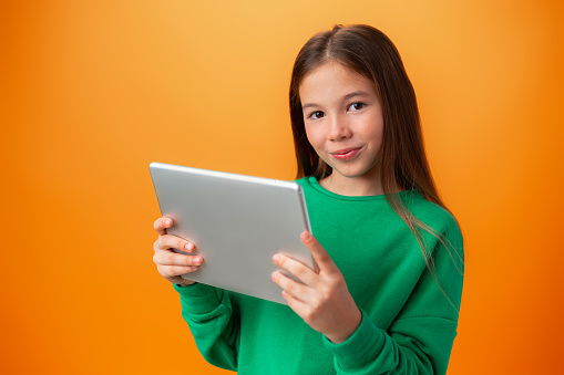 Beautiful teen girl using digital tablet over orange studio background, close up