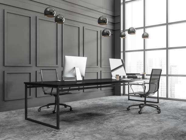 istock Coroner view of dark grey modern office space interior with two workplaces with desktops on desks and panoramic window with Singapore skyscrapers city view 1373419655