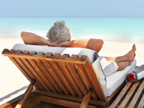 Rear-view of a mature guy relaxing on a deck chair at the beach