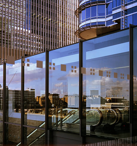 A modern skyscraper in Canary Wharf is the background of a smaller building with a glass facade that contains the reflections of the houses being built on the other side of the river. Photo'd circa 2005. A modern skyscraper in Canary Wharf is the background of a smaller building with glass facade that contains the reflections of the houses on the other side of the water.
