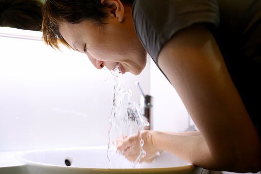 An Asian woman is rinsing her mouth in the bathroom.