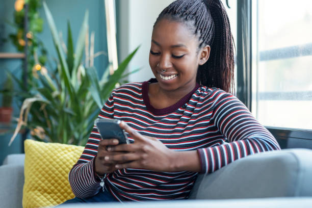 istock Smiling young african american woman using her mobile phone while sitting on sofa at home 1373451392