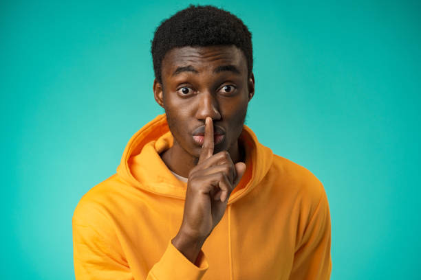 Black man showing silence gesture with finger on his lips Black man showing silence gesture with finger on his lips in studio finger on lips stock pictures, royalty-free photos & images