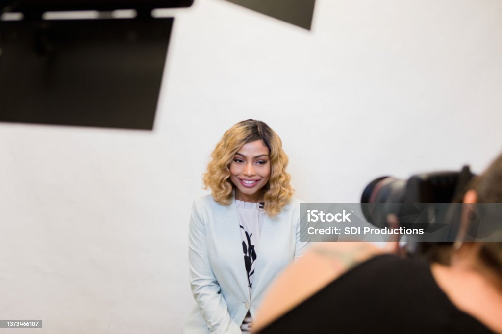 Female television host smiles as photographer takes headshots The mid adult female television host smiles as the unrecognizable female photographer takes publicity photos for the studio. Headshot Stock Photo