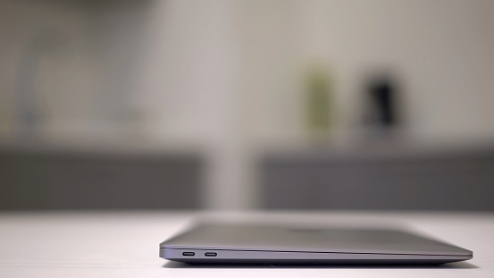 Person closes the laptop. Unrecognizable woman has finished working on the computer. Electronic device, tablet on the table in the kitchen. Remote work or study from home. USB type C ports.