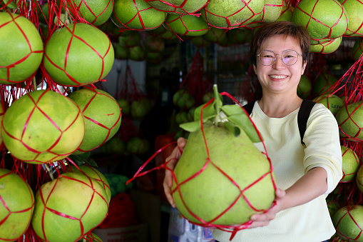 An Asian woman is feeling cheerful at fresh pomelo fruits business store.