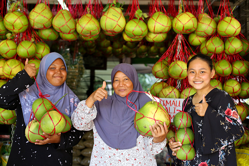 A Muslim store owners selling fresh pomelo fruits cheerfully.