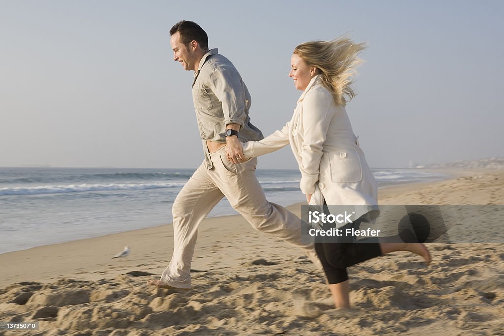 Happy couple running on beach A young male and female couple run holding hands on the beach. Adult Stock Photo