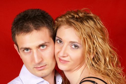 Beautiful young couple in love looking at camera over a red background. Selective focus.
