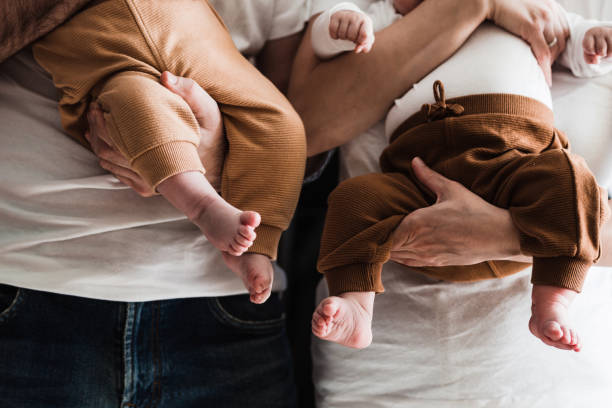 primo piano delle gambe e dei piedi del bambino nelle mani dei genitori - twin newborn baby baby girls foto e immagini stock