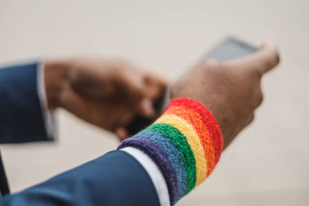 close-up of dark skinned hands with smartphone and lgbt bracelet outdoors . lgbtqia culture. - homosexual gay pride business rainbow imagens e fotografias de stock