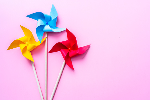 Close up view of multi colored pinwheels shot on pink background. The composition is at the left of an horizontal frame leaving useful copy space for text and/or logo at the right. High resolution 42Mp studio digital capture taken with SONY A7rII and Zeiss Batis 40mm F2.0 CF lens