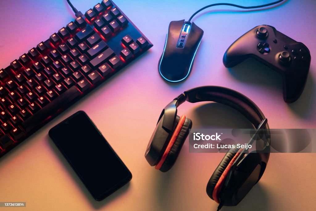 Gamer work space concept. gaming set up. top view of a gaming gear, keyboard, mouse, gamepad, joystick, headset and a smartphone on a colorful desk Headset Stock Photo