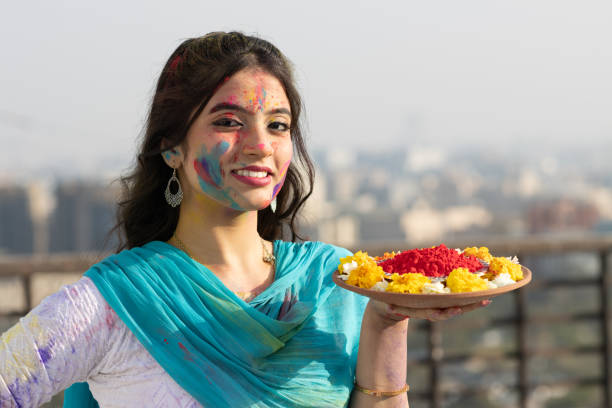 Young smart indian girl with plate full of color powder and face coloured with gulal for festival of colours Holi, a popular hindu festival celebrated across india stock photo