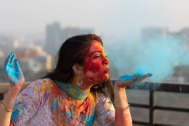 Pretty Young indian smart girl with face coloured with gulal for festival of colours Holi blowing holi color powder, a popular hindu festival celebrated across india stock photo
