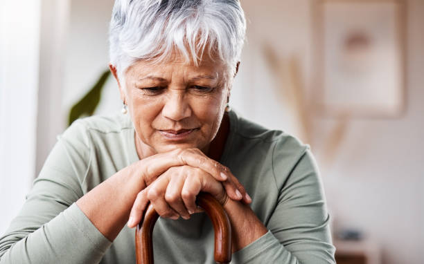 scatto di una donna anziana appoggiata al suo bastone da passeggio a casa - senior women depression sadness women foto e immagini stock