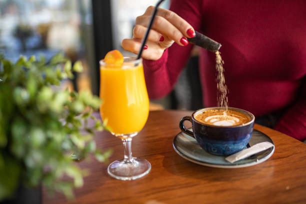 Woman adding sugar to her cappuccino in coffee shop stock photo