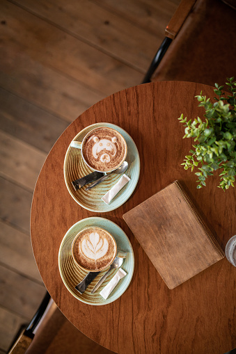 Two cups of fresh coffee with latte art on wooden table in coffee shop, directly above shot