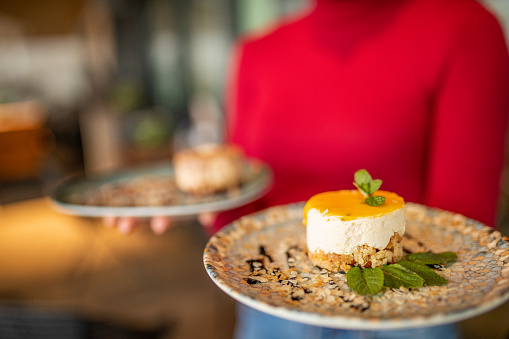 Unrecognizable waitress carrying two delicious cakes on plate in cafe