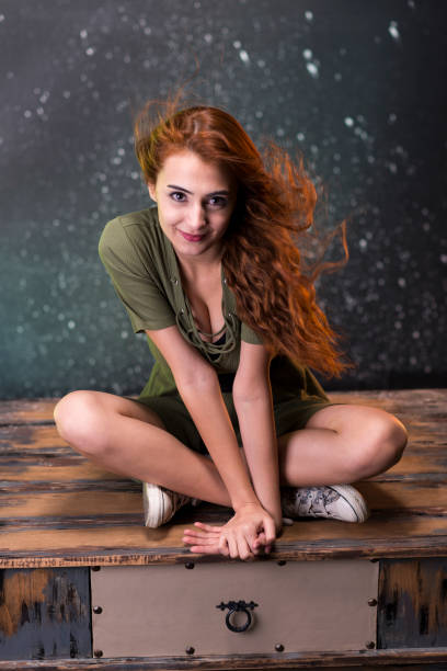 Cute young girl looking at camera smiling.\nYoung girl portrait in artistic tones achieved with aged backdrop and colored light.