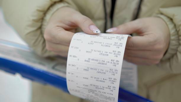 The buyer holds a purchase receipt in his hands, checks purchases and prices The buyer holds a purchase receipt in his hands, checks purchases and prices. Woman in a supermarket with a shopping cart. Girl with paper bill in store. receipt stock pictures, royalty-free photos & images