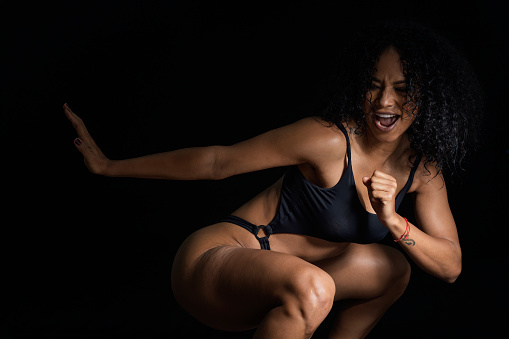 Latin woman with afro hair and skin of the average age of 25 years is photographed with small clothes showing the camera her muscular and defined athletic body in a photographic studio with a black background