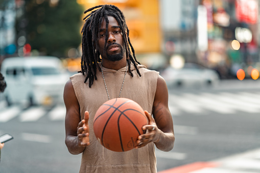 A portrait of a handsome Black-ethnicity man with a basketball in the city.