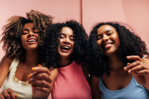 Three happy girlfriends with curly hair laughing together and looking at camera stock photo