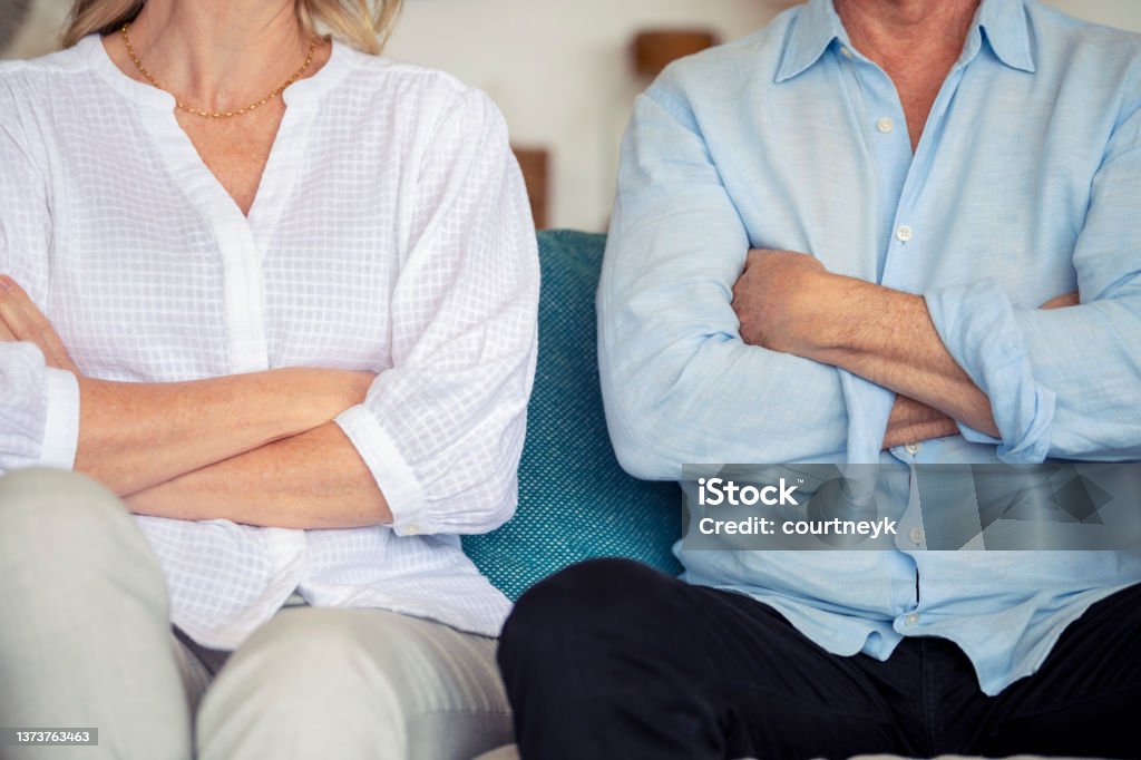 Mature couple fighting at home sitting on the sofa. Mature couple fighting at home sitting on the sofa. They are both looking angry and have their arms crossed Divorce Stock Photo