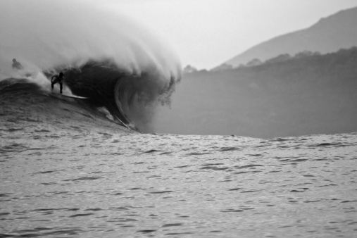 Some surfers in a HUGE wave in the morning. Black and white to show the cold of the morning.