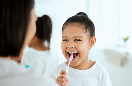 Shot of an adorable little girl  brushing her teeth while her mother helps her at home