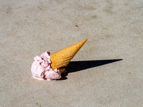 Dropped Strawberry ice cream cone melting on the sidewalk.