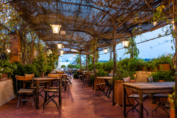 Typical Italian rooftop restaurant wooden tables in Tuscany with covered roof pergola vine canopy with empty seats, chairs and nobody in rustic romantic architecture stock photo