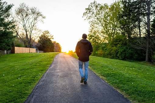 Caminata Sugarland Run Stream Valley Trail en Herndon, condado de Fairfax en la primavera de Virginia con camino pavimentado y silueta del hombre caminando hacia la puesta de sol como concepto de esperanza photo