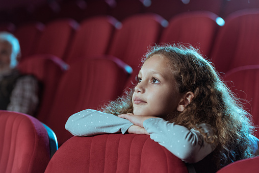 Little girl with curly hair in cinema watching movie
