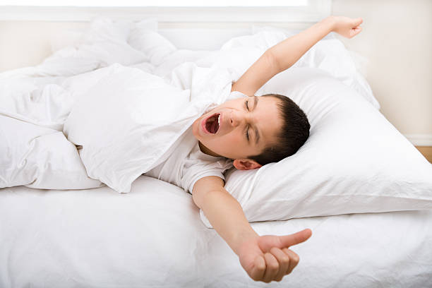 petit garçon bâillement et d'étirement au lit - pillow wake up yawning sleeping photos et images de collection
