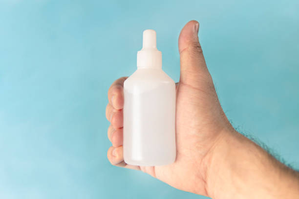 A white man's hand holding a medicine in a white bottle with an empty label. copy space for design and text la mano de una mujer blanca que sostiene un medicamento utilizado para despejar las vías respiratorias. solución aplicada directamente a la nariz con clorhidrato de oximetazolina como su compuesto principal. contiene 15 mililitros en botella.