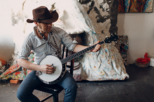 Male musician playing banjo sitting chair indoor.