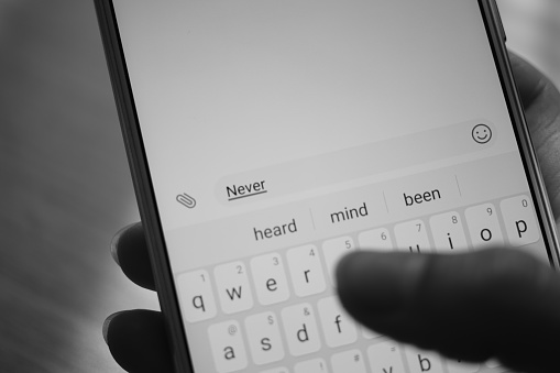 Human fingers typing on a smartphone screen a message Never. BW photo
