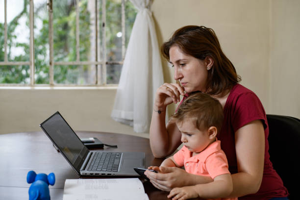 mother works while son sitting on her lap watches cartoons on her mobile phone - multi ethnic group concentration mobile phone using laptop imagens e fotografias de stock