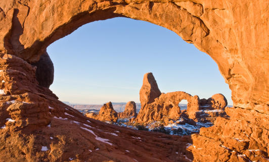 Utah's winter sun rises on Turret Arch through North Window in Arches National Park.