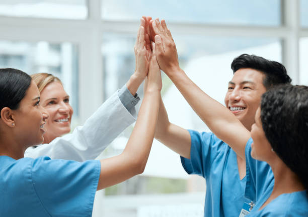 shot of a group of medical practitioners joining hands to high five each other at work - changing form imagens e fotografias de stock