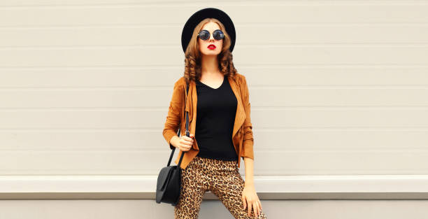 istock Beautiful stylish woman model wearing black round hat, brown jacket and handbag on gray background 1374016607