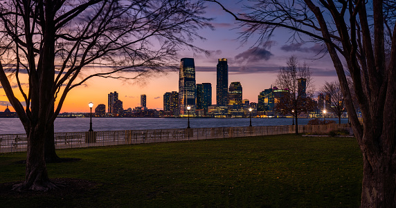 Panoramic evening view of Downtown Jersey City skyscrapers across the Hudson River. Riverfront at twilight from Battery Park (Lower Manhattan). New York City