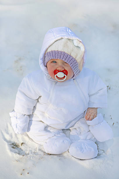 baby in the first snow adorable little baby bundled up in white snow suit with a red pacifier rosy cheeks stock pictures, royalty-free photos & images