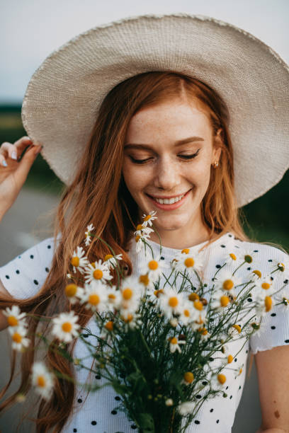 Portrait of a caucasian red-haired woman in hat holding a daisies bouquet. Closeup portrait. Beautiful young girl. Chamomile flower field. stock photo